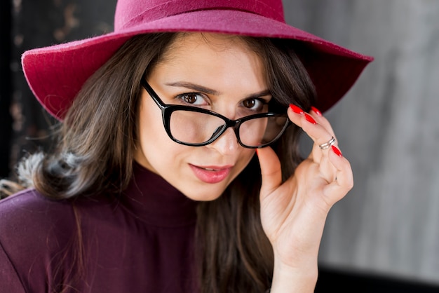 Close-up portrait of young beautiful fashionable woman with eyeglasses and hat over her head