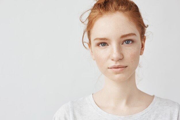 Close up portrait of young beautiful redhead woman in white shirt smiling