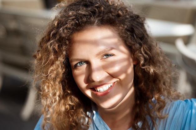 Close up portrait of young beautiful smiling girl sitting at cafe in sun rays.