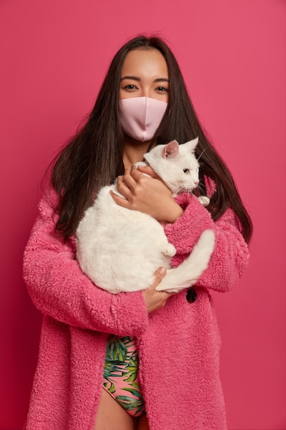 Close up portrait of young beautiful woman with protective mask holding a cat isolated
