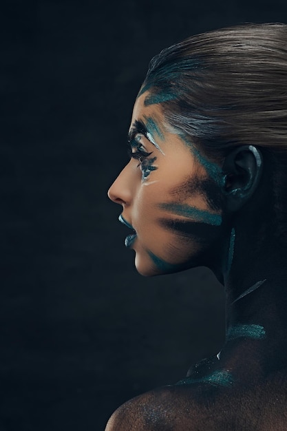 創造的なメイクアップの若い美女のクローズアップの肖像画。彼女の顔に青と黒の影が描かれています。概念的なアイデア。