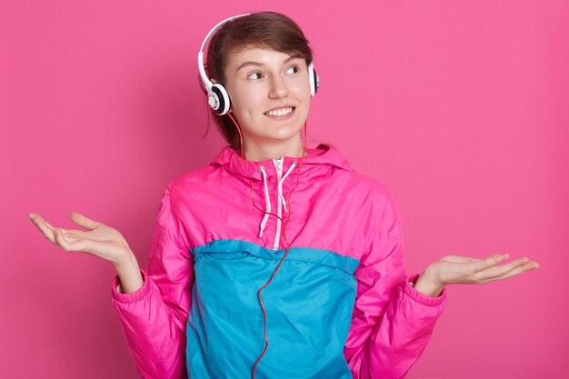 Close up portrait of young brunette with headphones on her head dressed in pink and blue sport shirt