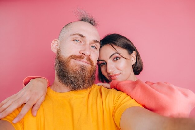 Close up portrait of young, caucasian, attractive, lovely, cute, sweet, smiling, positive couple in casual making selfie on mobile phone on pink background