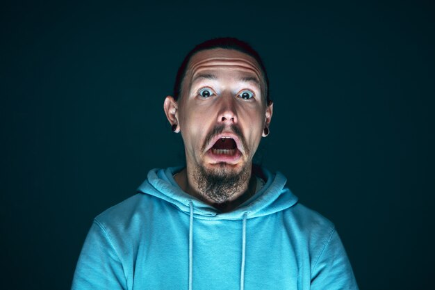 Close up portrait of young crazy scared and shocked caucasian man isolated on dark background.