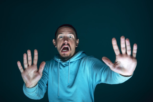 Close up portrait of young crazy scared and shocked caucasian man isolated on dark background.