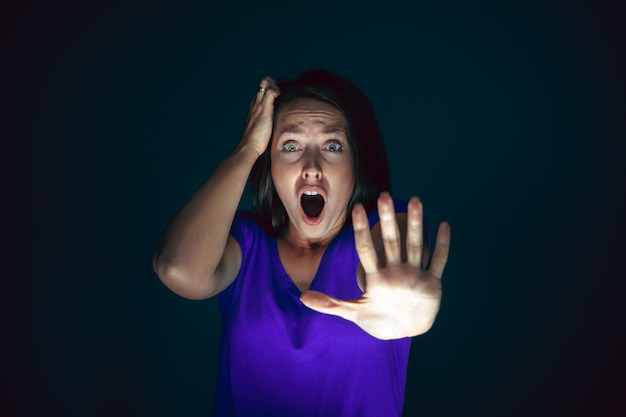 Close up portrait of young crazy scared and shocked woman isolated on dark
