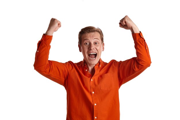 Close-up portrait of a young excited ginger male in a stylish orange shirt acting like he is overjoyed about something while posing isolated on white studio background. Human facial expressions. Since