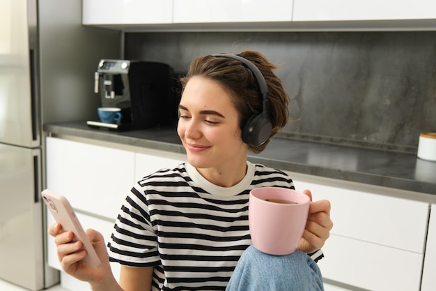 Free photo close up portrait of young female student drinking tea and listening to music in headphones using