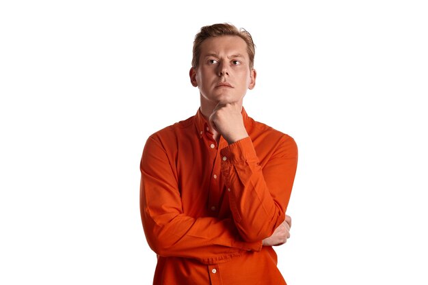 Close-up portrait of a young goodly ginger fellow in a stylish orange shirt looking thoughtful while posing isolated on white studio background. Human facial expressions. Sincere emotions concept. Cop