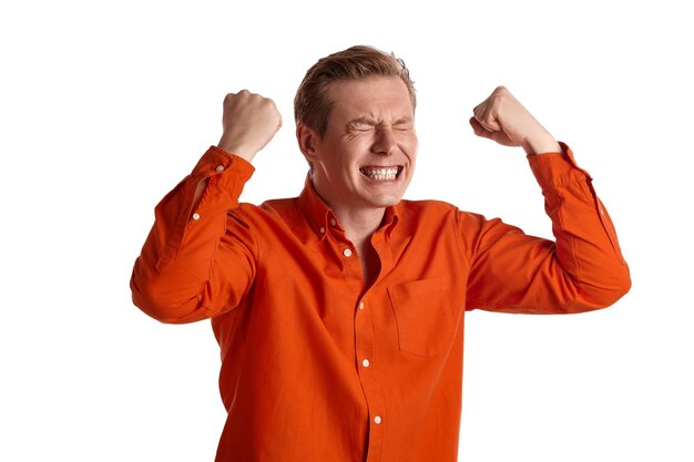 Close-up portrait of a young goodly ginger guy in a stylish orange shirt acting like he is overjoyed about something while posing isolated on white studio background. Human facial expressions. Sincere