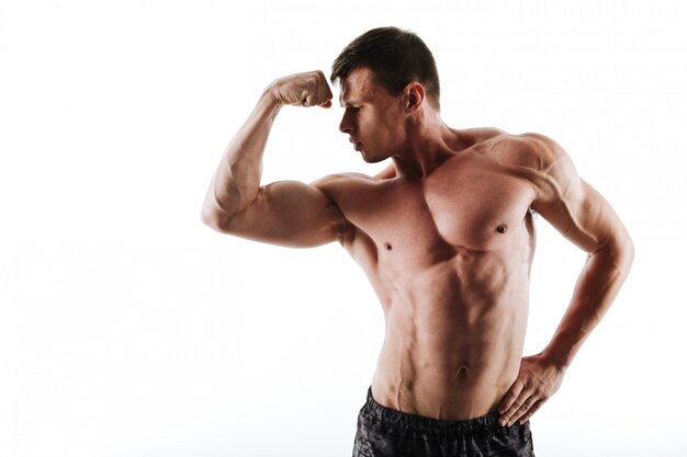 Close-up portrait of young half naked bodybuilder looking at his biceps