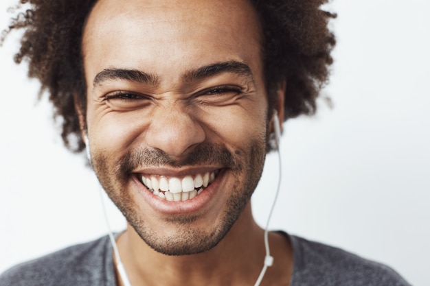 Chiuda sul ritratto di giovane uomo africano felice che sorride ascoltando la risata ottimistica di musica in streaming. concetto di gioventù.