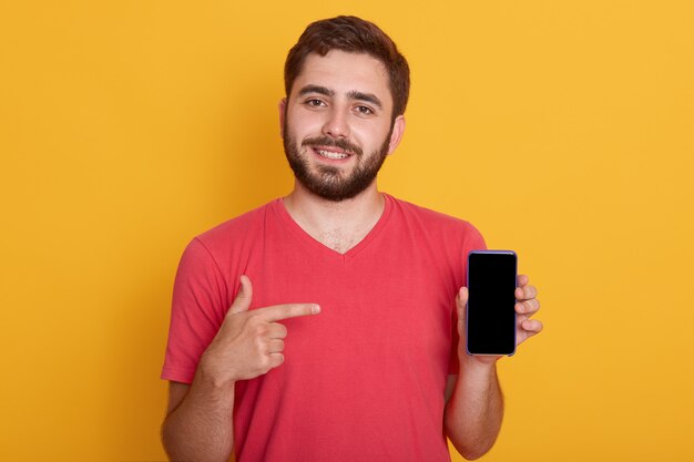 Close up portrait of young happy man in red shirt showing black blank smart phone screen