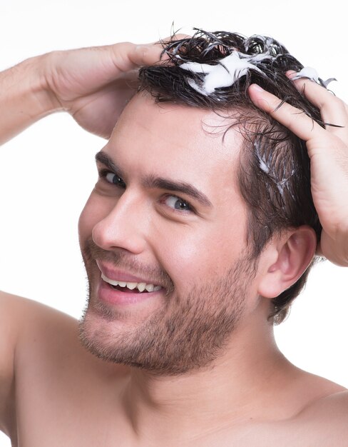 シャンプーで髪を洗うクローズアップの肖像画の若い幸せな笑顔の男-白で隔離。