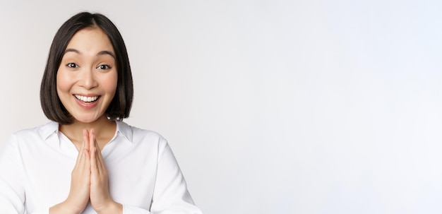 Close up portrait of young japanese woman showing namaste thank you arigatou gesture standing over w