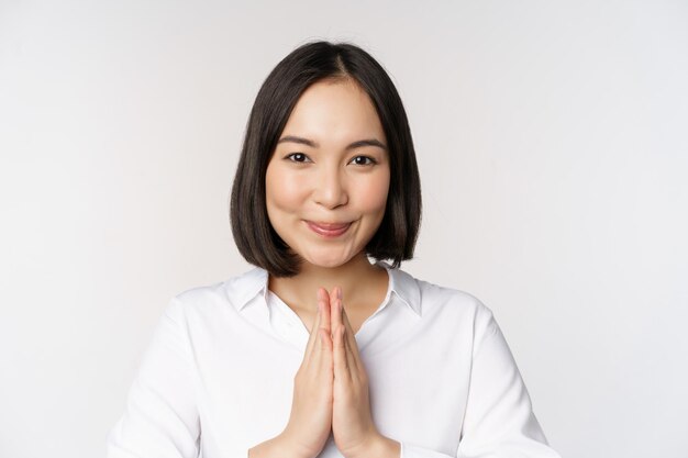 Close up portrait of young japanese woman showing namaste thank you arigatou gesture standing over white background