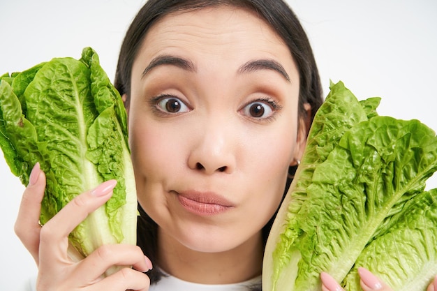 Free photo close up portrait of young korean woman holds lettuce next to healthy natural face without blemishes