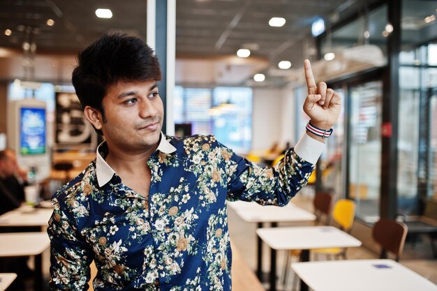 Крупный план портрета молодого индийского фрилансера в кафе быстрого питания красивый мужчина в рубашке в удобной кофейне показывает пальцем вверх знак