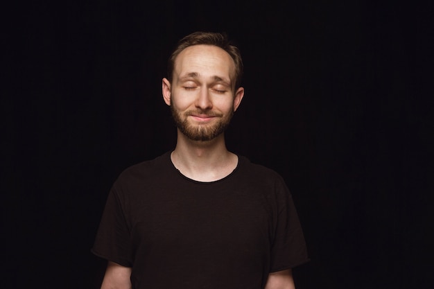 Free photo close up portrait of young man isolated on black  space.  thinking and smiling