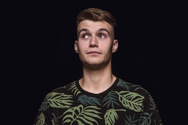 Close up portrait of young man isolated on black studio background. Photoshot of real emotions of male model. Dreaming and smiling, hopeful and happy. Facial expression, human emotions concept.