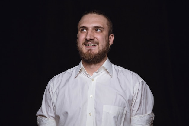 Close up portrait of young man isolated on black studio background. Photoshot of real emotions of male model. Dreaming and smiling, hopeful and happy. Facial expression, human emotions concept.