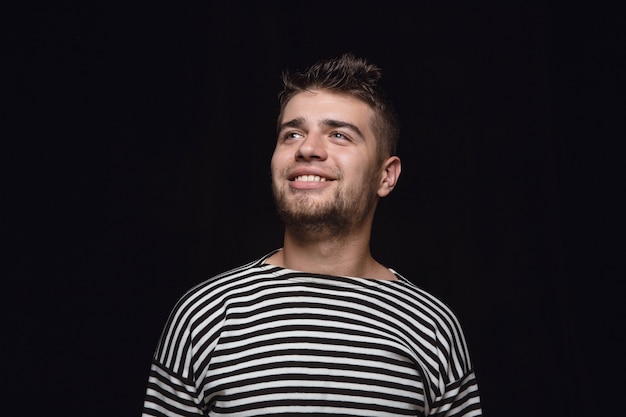 Close up portrait of young man isolated on black studio background. Photoshot of real emotions of male model. Dreaming and smiling, hopeful and happy. Facial expression, human emotions concept.