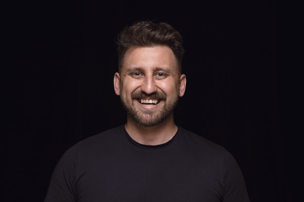 Close up portrait of young man isolated on black studio background. Photoshot of real emotions of male model. Smiling, feeling crazy happy, laughting. Facial expression, human emotions concept.