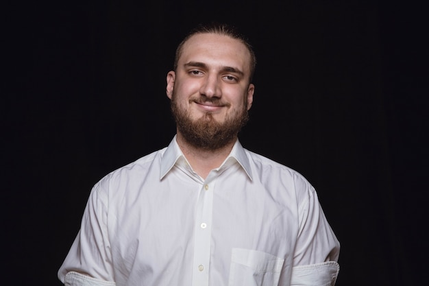 Close up portrait of young man isolated on black studio background. Photoshot of real emotions of male model. Smiling, feeling happy. Facial expression, pure and clear human emotions concept.