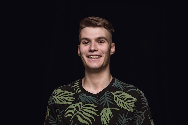 Close up portrait of young man isolated on black studio background. Photoshot of real emotions of male model. Smiling, feeling happy. Facial expression, pure and clear human emotions concept.