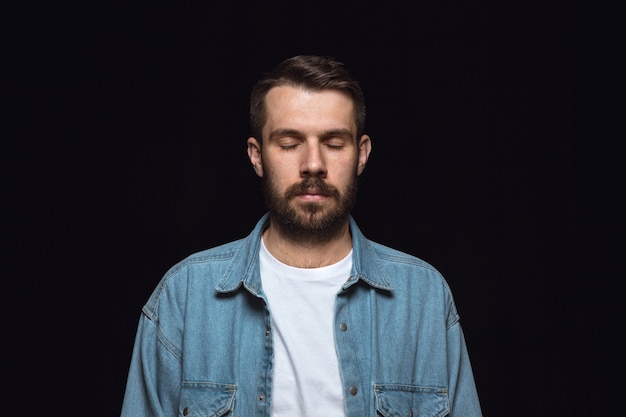 Close up portrait of young man isolated on black studio background. Photoshot of real emotions of male model with closed eyes. Thoughtful. Facial expression, human nature and emotions concept.