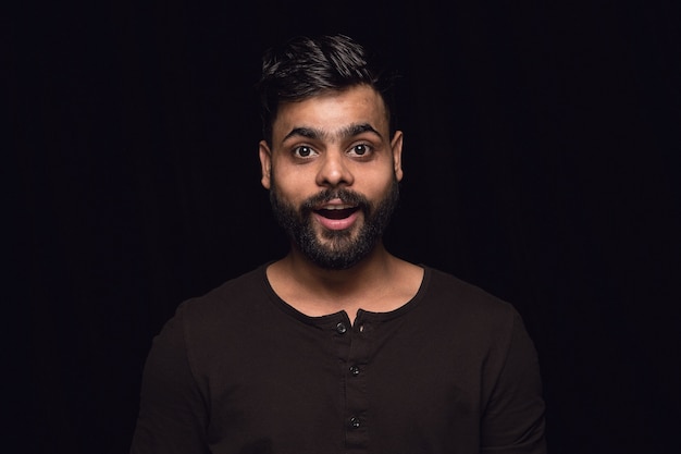 Close up portrait of young man isolated on black studio background. Wondering, exciting and astonished.