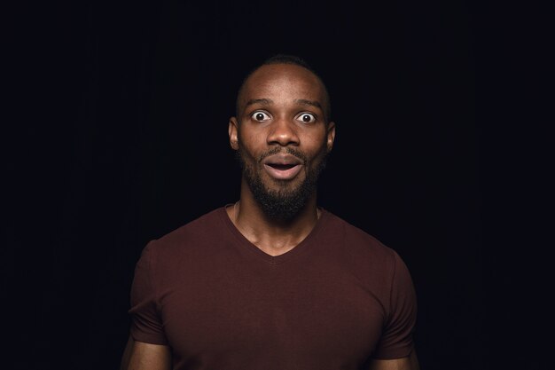 Close up portrait of young man isolated on black studio wall. Wondering, exciting and astonished.