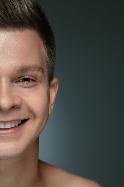Close-up portrait of young man isolated on grey  background. Caucasian male model looking directly and posing, smiling.