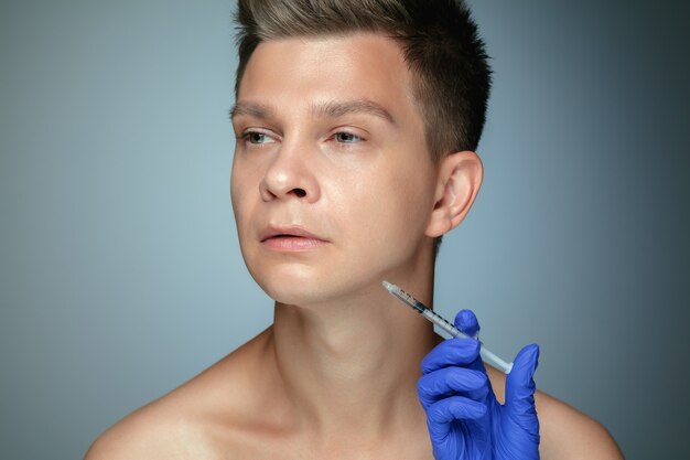 회색 배경에 고립 된 젊은 남자의 클로즈업 초상화. 충전 수술 절차, 입술 및 광대뼈.