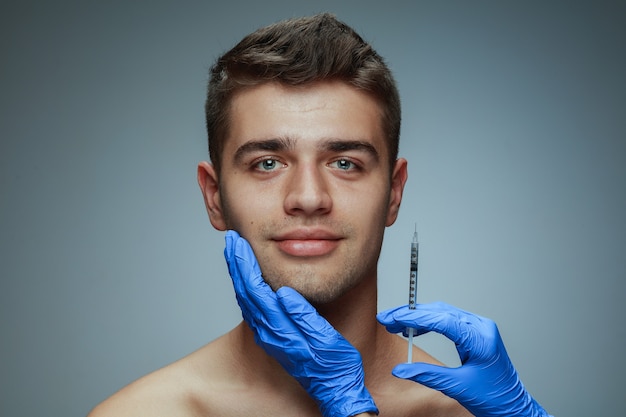 회색 배경에 고립 된 젊은 남자의 클로즈업 초상화. 충전 수술 절차.