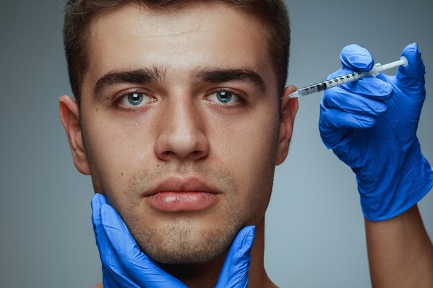 Close-up portrait of young man isolated on grey  background. Filling surgery procedure.