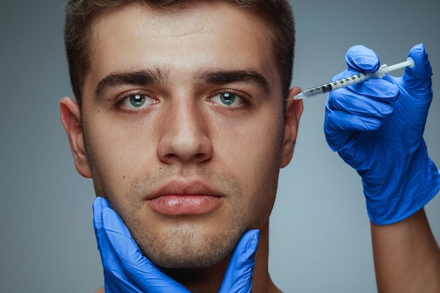 Close-up portrait of young man isolated on grey  background. Filling surgery procedure.