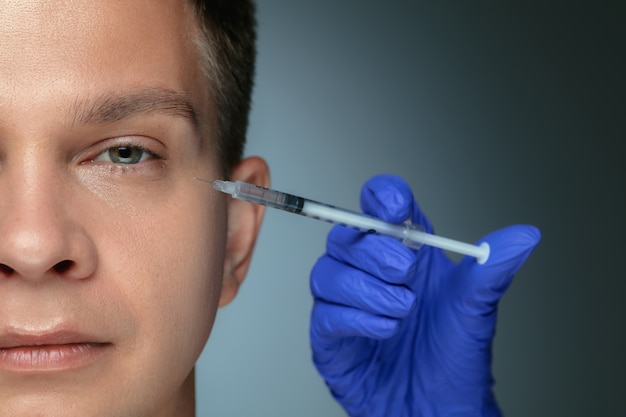 Close-up portrait of young man isolated on grey  background. Filling surgery procedure.