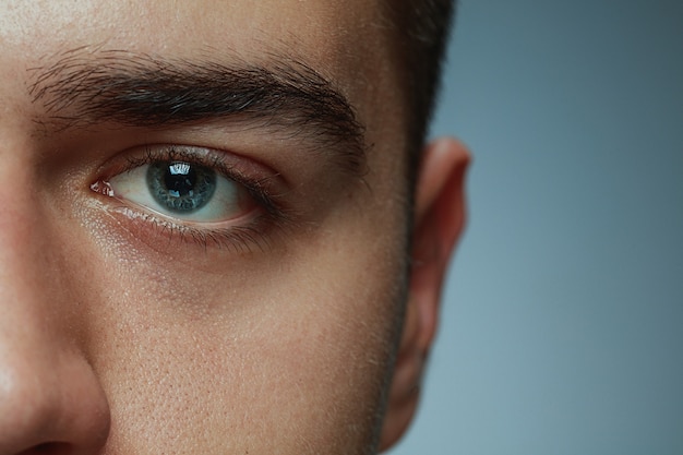 Close-up portrait of young man isolated on grey studio background. Caucasian male model's face and blue eye. Concept of men's health and beauty, self-care, body and skin care, medicine or phycology.