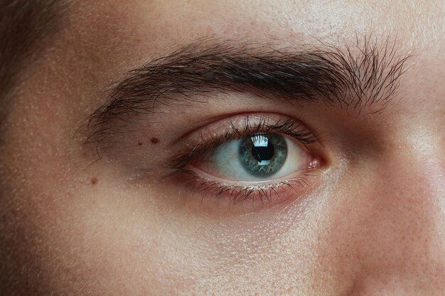 Close-up portrait of young man isolated on grey studio background. Caucasian male model's face and blue eye. Concept of men's health and beauty, self-care, body and skin care, medicine or phycology.