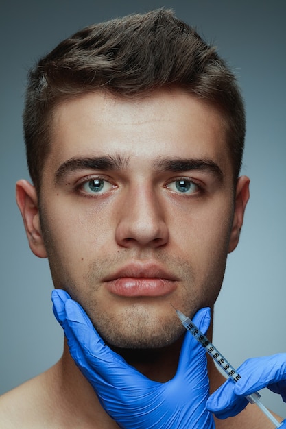 Close-up ritratto di giovane uomo isolato su grigio di sfondo per studio. procedura chirurgica di riempimento. concetto di salute e bellezza maschile, cosmetologia, cura di sé, cura del corpo e della pelle. anti età.