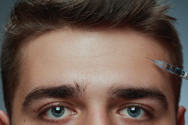 Close-up portrait of young man isolated on grey studio background. Filling surgery procedure. Concept of men's health and beauty, cosmetology, self-care, body and skin care. Anti-aging.