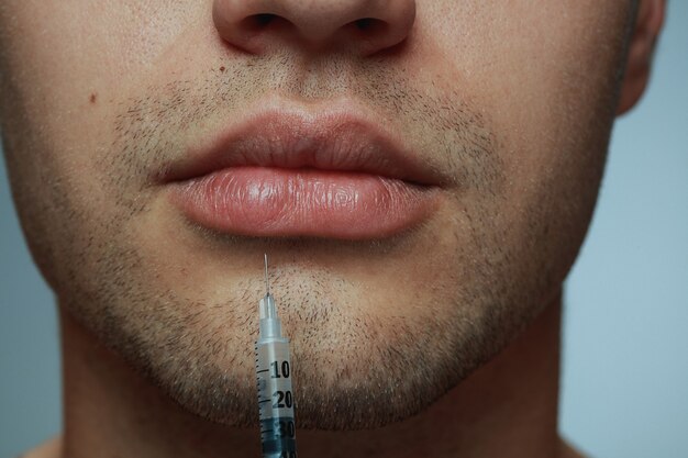 Close-up portrait of young man isolated on grey studio background. Filling surgery procedure. Concept of men's health and beauty, cosmetology, self-care, body and skin care. Anti-aging.