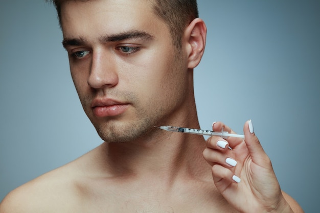 Close-up portrait of young man isolated on grey studio background. filling surgery procedure. concept of men's health and beauty, cosmetology, self-care, body and skin care. anti-aging.