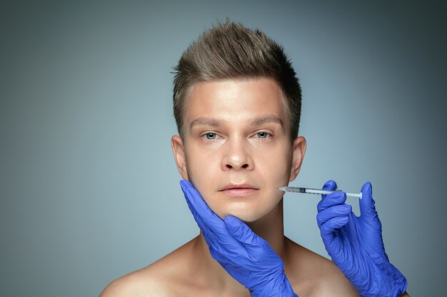 Close-up portrait of young man isolated on grey studio wall in filling surgery procedure