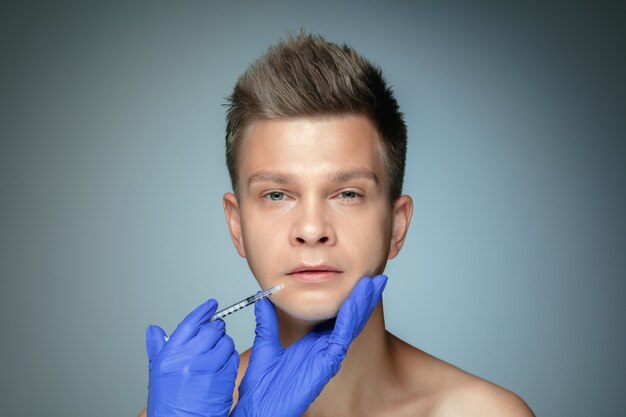 Close-up portrait of young man isolated on grey studio wall in filling surgery procedure