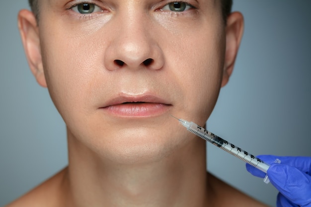 Close-up portrait of young man isolated on grey studio wall in filling surgery procedure