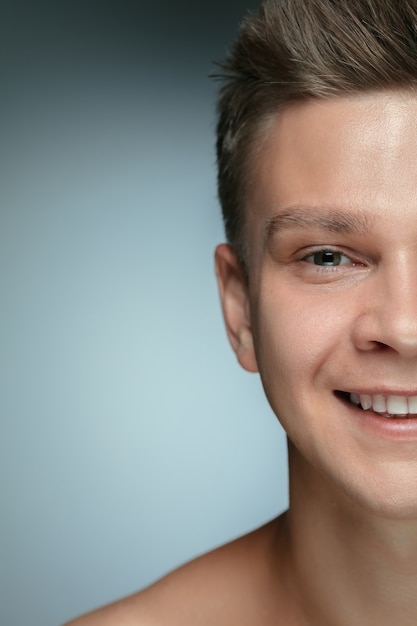 Free photo close-up portrait of young man isolated on grey  wall. caucasian male model looking at camera and posing, smiling. concept of men's health and beauty, self-care, body and skin care.