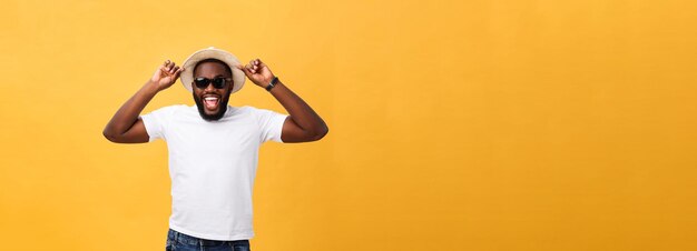 Close up portrait of a young man laughing with hands holding hat isolate over yellow background