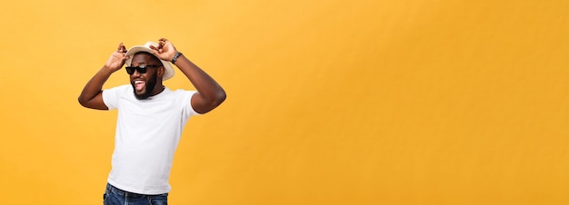 Close up portrait of a young man laughing with hands holding hat isolate over yellow background